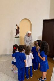 Irmã com crianças da Educação Infantil diante da imagem do Sagrado Coração
